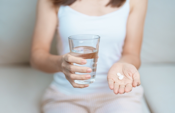 vrouw met antibioticapillen en glas water in de handen